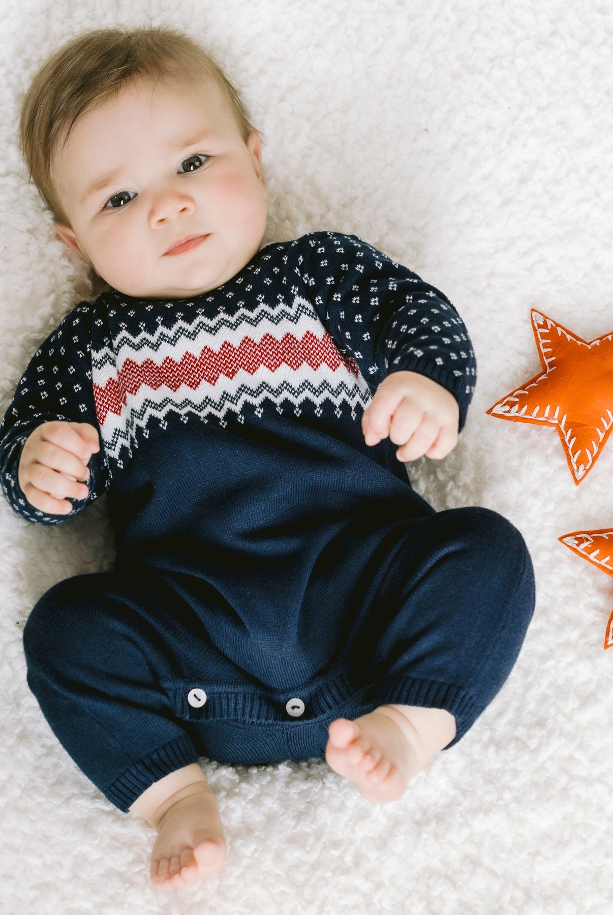 Baby lying on a textured surface with two orange stars nearby
