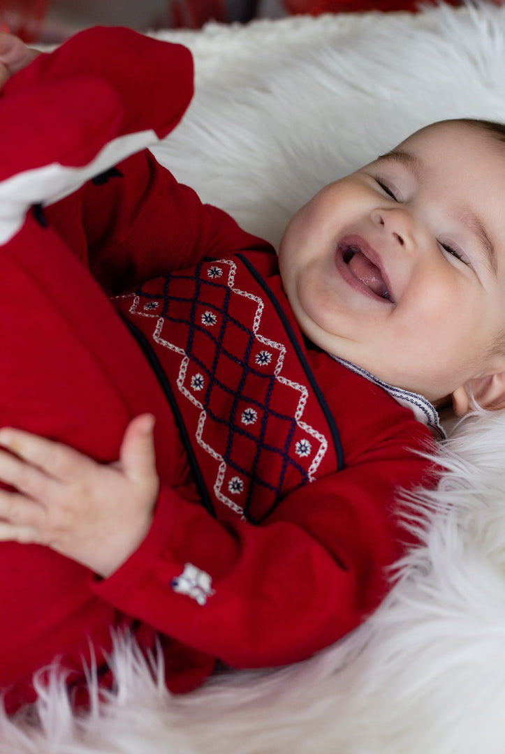 Baby in a red outfit lying on a white fluffy surface