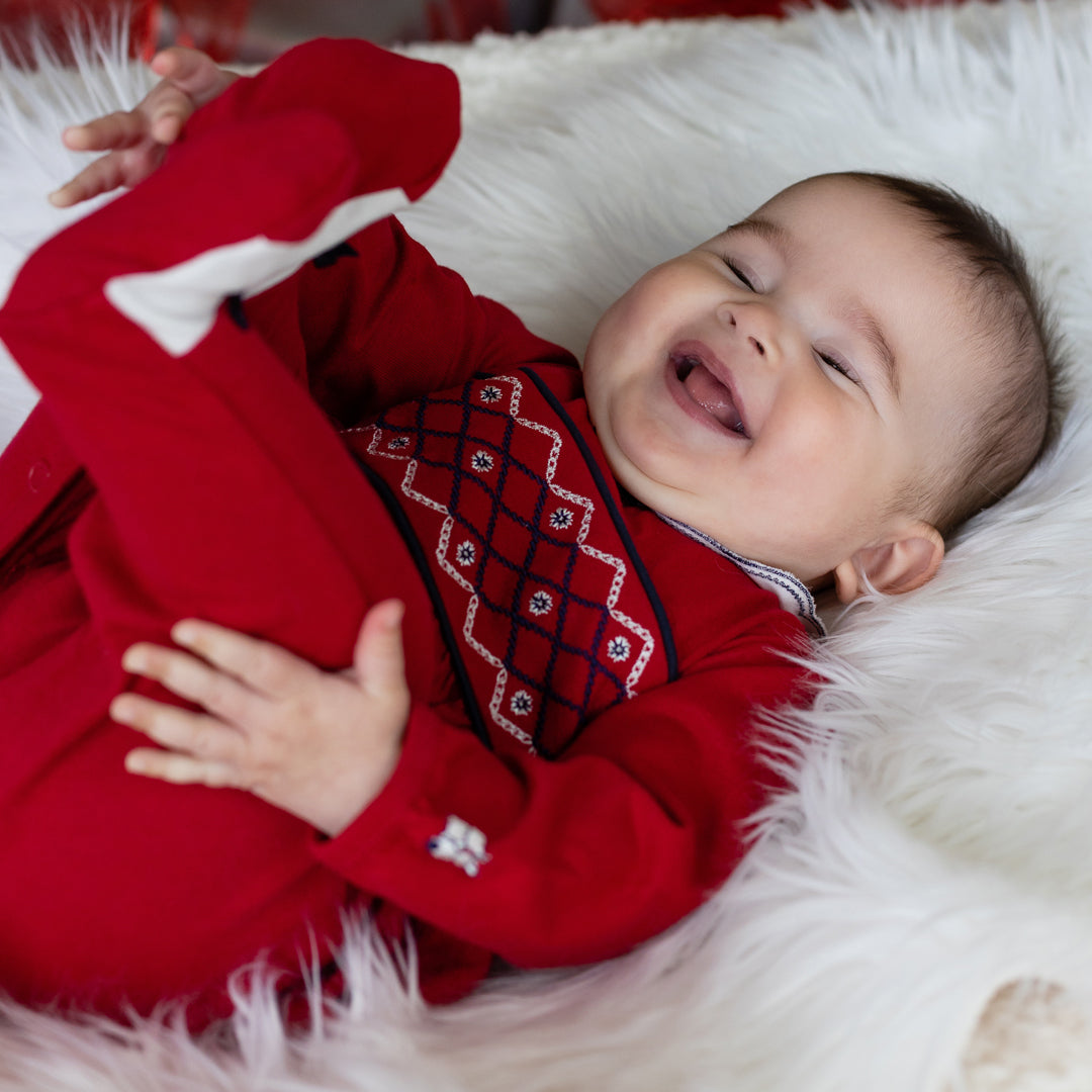 Baby in a red outfit lying on a white fluffy surface