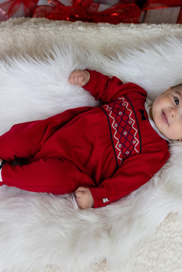 Baby in a red outfit with a pattern lying on a white fluffy surface
