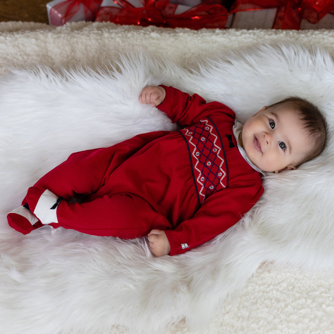 Baby in a red outfit with a pattern lying on a white fluffy surface