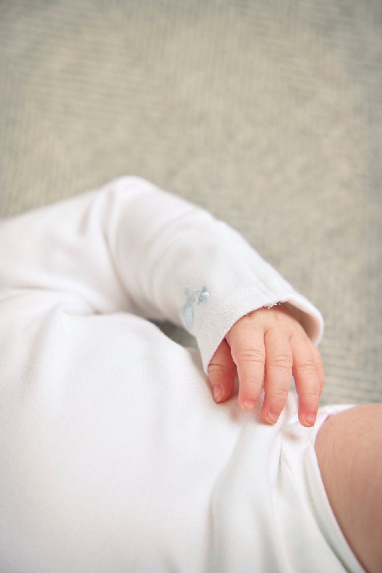 Close-up of a baby's hand and arm wearing a white long-sleeve shirt on a neutral background