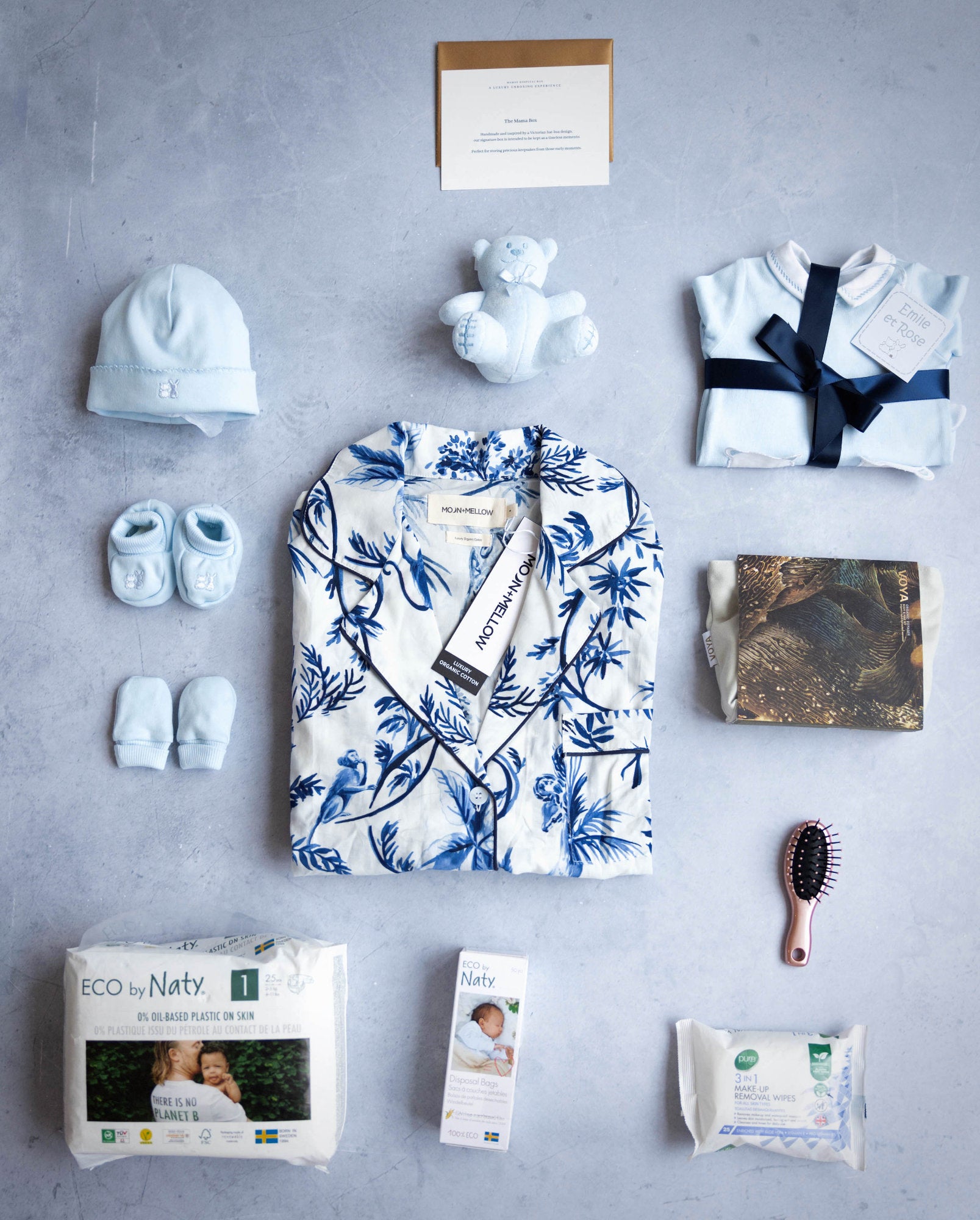 A set of baby and maternity related items in blue, including a nightdress, baby clothes, a matching hat, a cuddly toy, a mini hair brush, nappies, wipes, and a keepsake box.