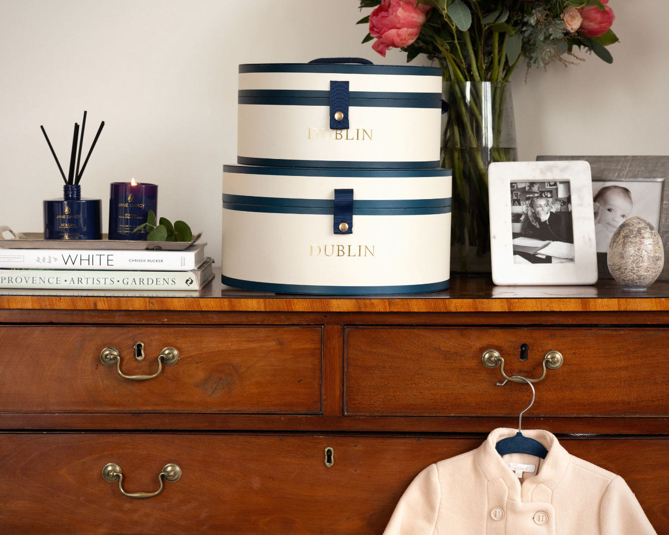 Wooden dresser with decorative hats, flowers, books, and a coat.
