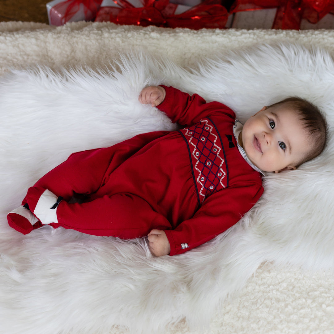 Baby in a red outfit with a pattern lying on a white fluffy surface.
