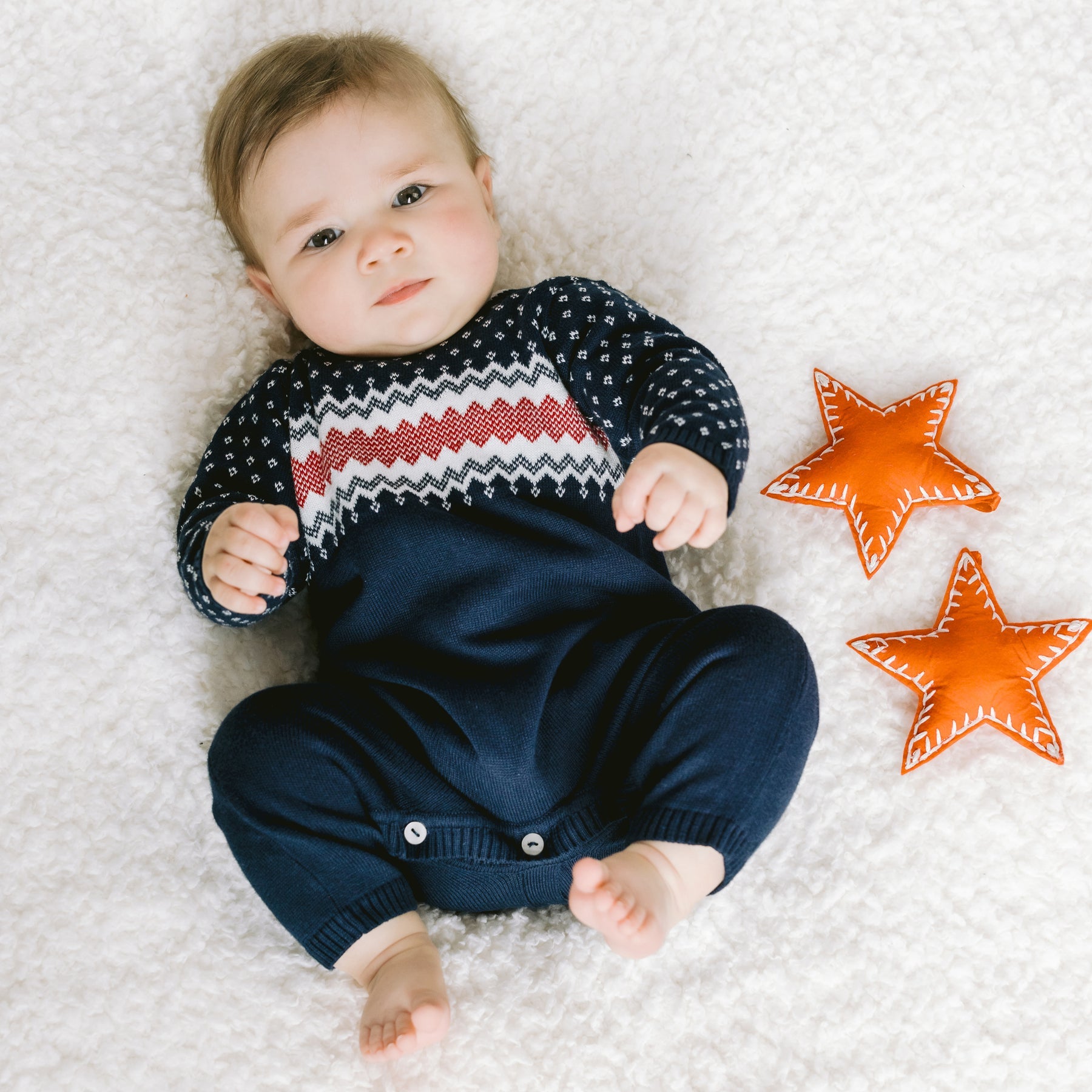 Baby lying on a textured surface with two orange stars nearby