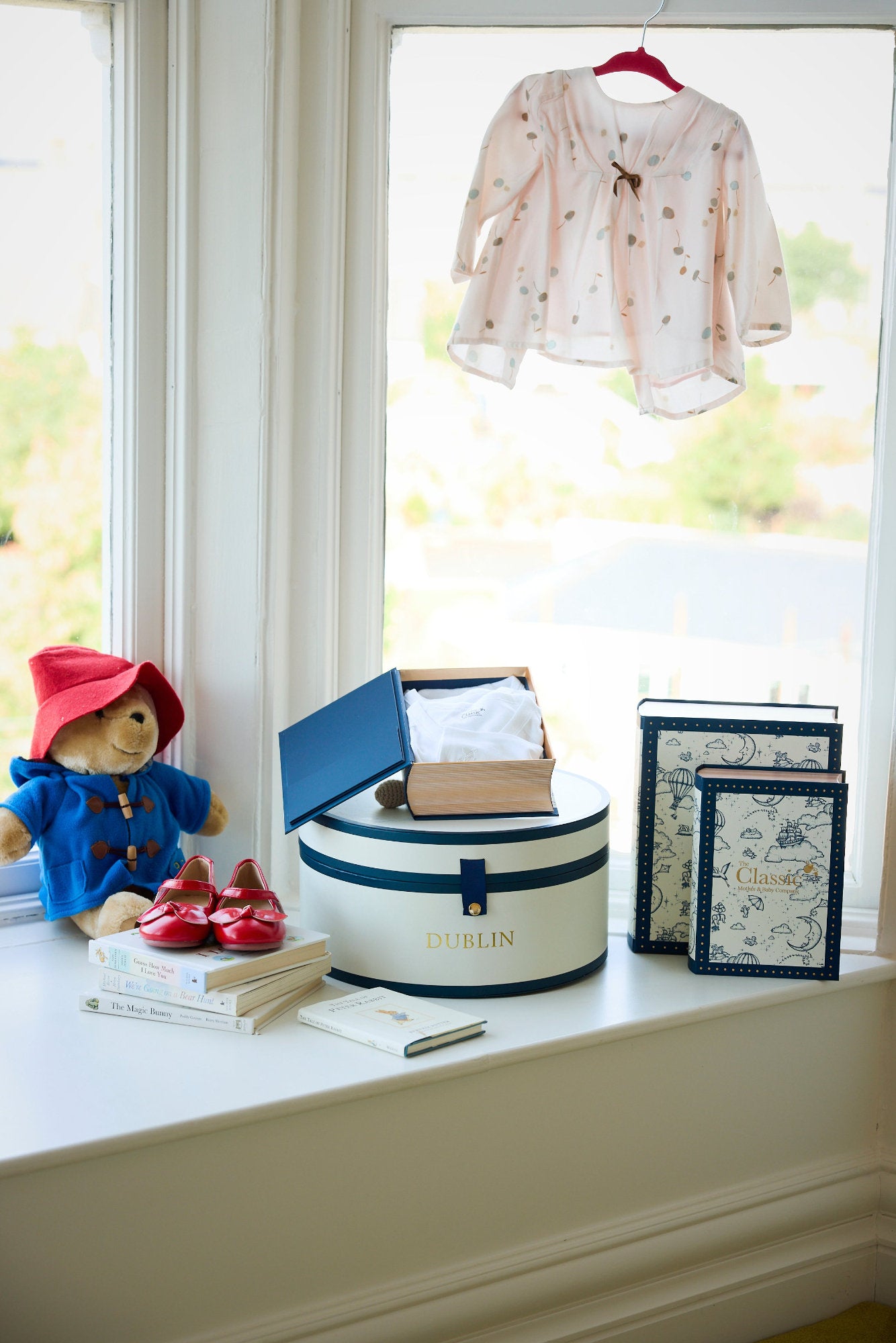 A set of baby clothes displayed next to a stuffed toy on a window sill, with organic cotton and bamboo materials visible.