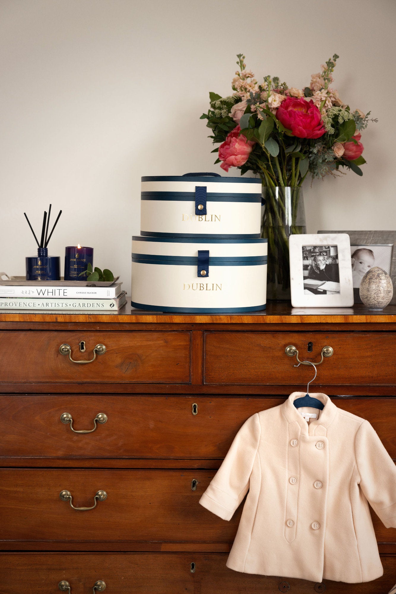 Wooden dresser with decorative hats, flowers, books, and a coat.