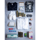 A collection of baby and maternity items including a nightdress, sleepshirts, pyjama set, eye cream, facecloths, facial set, shower gel, shampoo and conditioner, body lotion, mama oil, hand cream, and a candle, displayed neatly on a grey background.